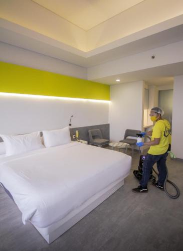 a man vacuum cleaning a hotel room with a large bed at YELLO Hotel Paskal Bandung in Bandung