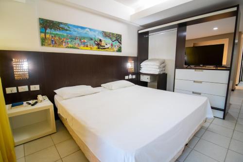 a bedroom with a large white bed and a flat screen tv at Flat Pipa's Bay in Pipa