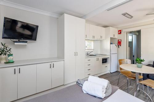 a kitchen with white cabinets and a table with a tv at Holiday Haven Burrill Lake in Burrill Lake