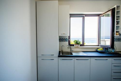 eine Küche mit weißen Schränken, einem Waschbecken und 2 Fenstern in der Unterkunft A casa da putìa, l'emozione di un tramonto in Milazzo