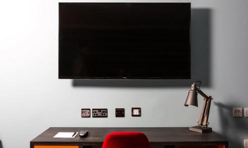a flat screen tv on a wall with a red chair at Village Hotel Aberdeen in Aberdeen