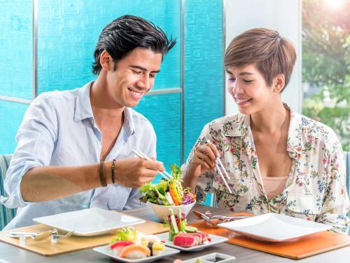 a man and woman sitting at a table eating food at Novotel Bangkok IMPACT in Nonthaburi