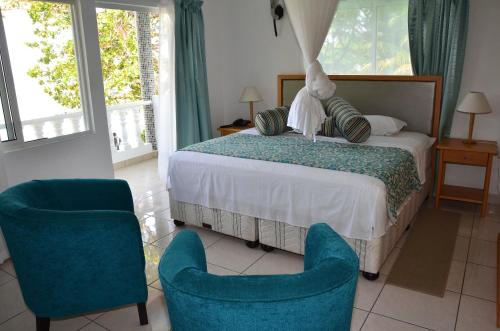 a bedroom with a bed and two blue chairs at Moonlight Beach Villa in La Digue