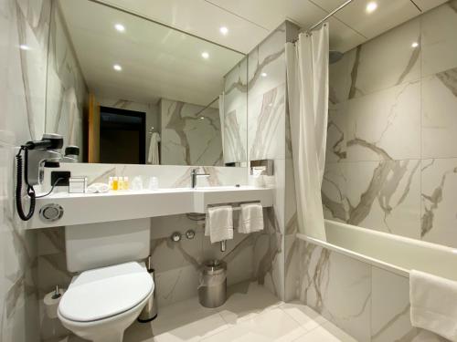 La salle de bains est pourvue de toilettes, d'un lavabo et d'une baignoire. dans l'établissement Nash Airport Hotel, à Genève
