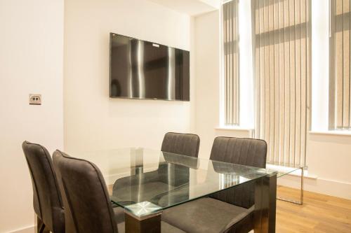 a glass table with chairs and a television on a wall at Lord Street Apartments By Happy Days in Liverpool