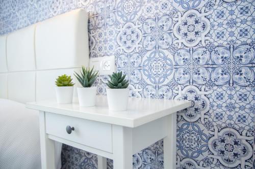 uma mesa branca com vasos de plantas sobre ela contra um papel de parede azul e branco em Casa Palacio Don Pedro em Sevilha