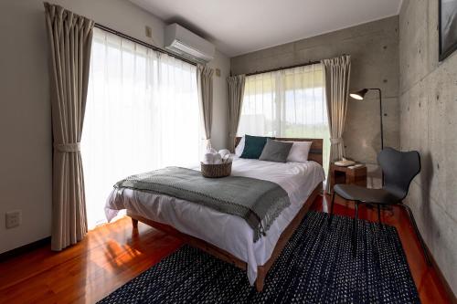 a bedroom with a bed and a chair and windows at LEO Resort Sunayama in Miyako Island