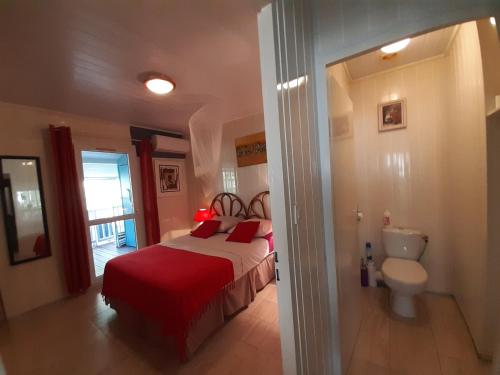 a bedroom with a bed with red sheets and a toilet at Les Gites Capra - Papaye in Bouillante