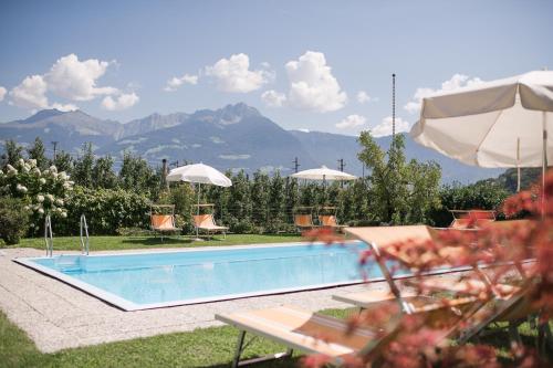 a swimming pool with chairs and umbrellas and mountains at Untermairhof B&B Christine in Lagundo