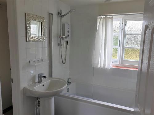 a white bathroom with a shower and a sink at Primrose Cottage in Moreton