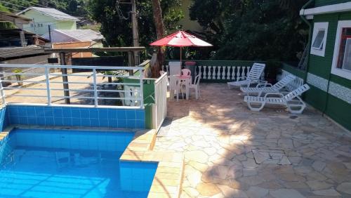 um pátio com cadeiras e um guarda-sol ao lado de uma piscina em Chales Virena em Ubatuba