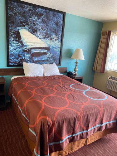 a bed in a hotel room with a large painting on the wall at Super 8 by Wyndham Midwest City OK in Midwest City