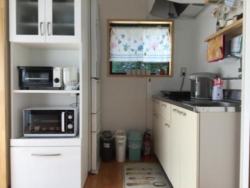 a small kitchen with white cabinets and a microwave at 民泊大森 in Iyo
