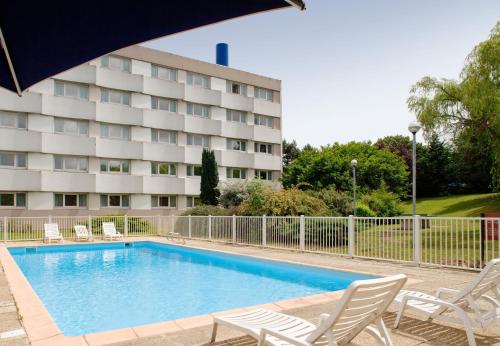a hotel swimming pool with chairs and an umbrella at Mercure Paris Le Bourget Aeroport in Le Blanc-Mesnil
