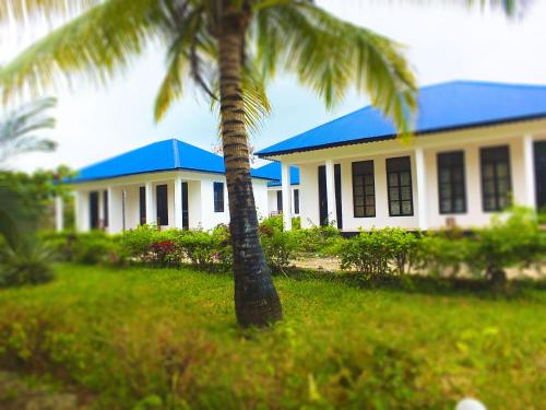 a white house with a blue roof and a palm tree at Kigwedeni Villas in Nungwi