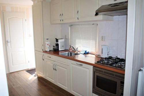 uma cozinha com armários brancos, um lavatório e um fogão em Resort Venetie Chalet nr.42 em Giethoorn
