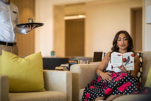 a woman sitting on a couch reading a book at InterContinental Fujairah Resort by IHG in Al Aqah