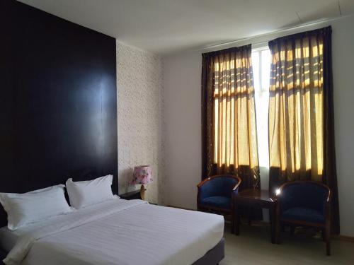 a bedroom with a bed and two chairs and a window at Ginasuite Hotel in Bandar Seri Begawan