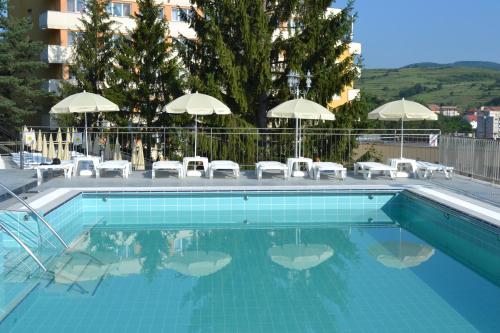 a swimming pool with chairs and umbrellas at Hotel Germisara in Geoagiu Băi