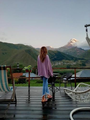 a woman standing on a deck looking at the mountains at Guesthouse Elli & Cottages in Stepantsminda