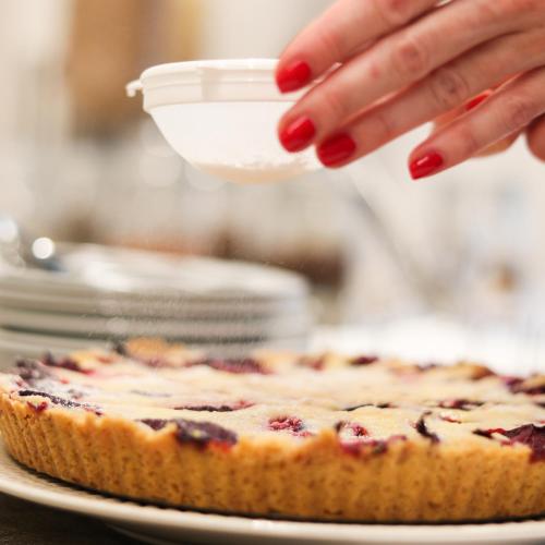 a woman with red fingernacs is pouring icing onto a blueberry pie at Hotel KOZÁK in Brno