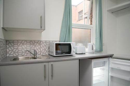 a kitchen counter with a microwave and a sink at TLK Apartments & Hotel - Beckenham High Street in Beckenham