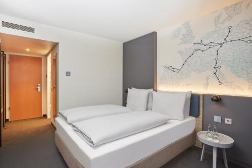 H4 Hotel Leipzig في لايبزيغ: غرفة نوم مع سرير أبيض مع خريطة على الحائط