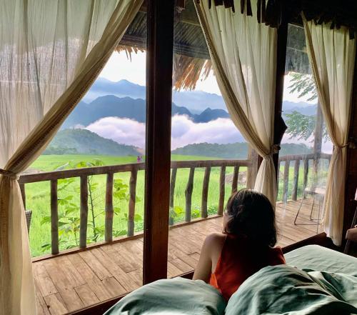 a woman sitting on a bed looking out of a window at Pu Luong Ecocharm in Hương Bá Thước