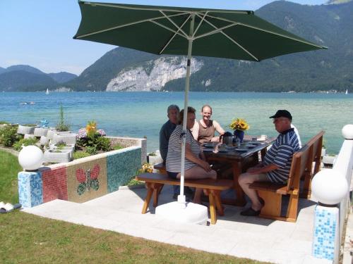 a group of people sitting at a table under an umbrella at Haus Seehof in Sankt Gilgen