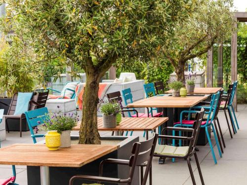eine Reihe von Tischen und Stühlen unter einem Orangenbaum in der Unterkunft Mercure Amsterdam City Hotel in Amsterdam