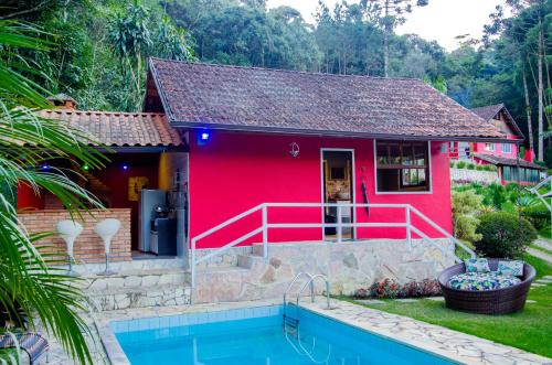 a red house with a swimming pool in front of it at Pousada Refúgio das Aves in Visconde De Maua