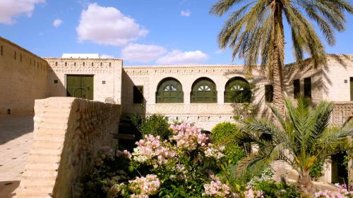 a building with a palm tree and flowers at DAR NEJMA in Tozeur