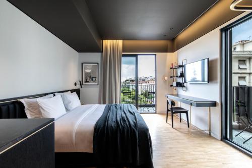 アテネにあるThe Modernist Athensのベッド、デスク、バルコニーが備わるホテルルームです。