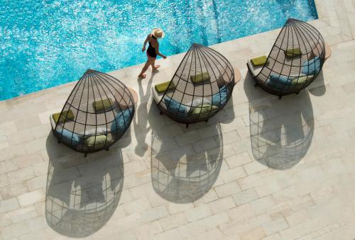 a woman walking by a pool with four chairs at RIMBA by AYANA Bali in Jimbaran