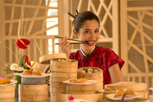 a woman holding a chopsticks in front of a table with food at RIMBA by AYANA Bali in Jimbaran