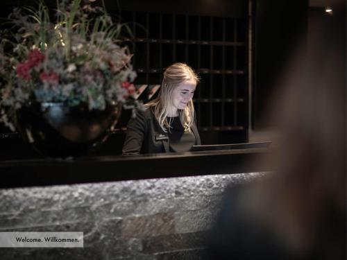 a young woman sitting at a window with flowers at Grischa - Das Hotel Davos in Davos