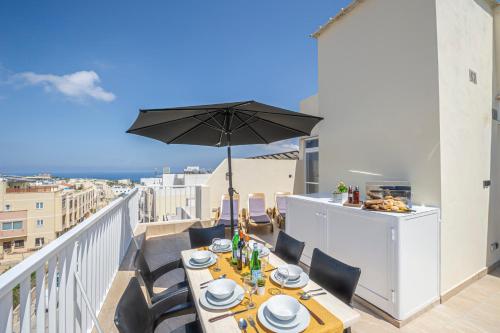 a table on a balcony with an umbrella at Summer Breeze Penthouse with private Hot Tub & terrace with panoramic views, by Getawaysmalta in Mellieħa