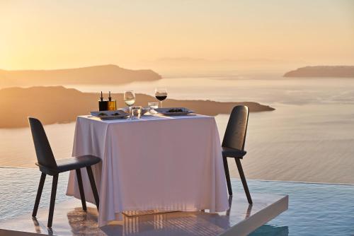 a table with two glasses of wine on top of the ocean at Alti Santorini Suites - Caldera View in Megalochori