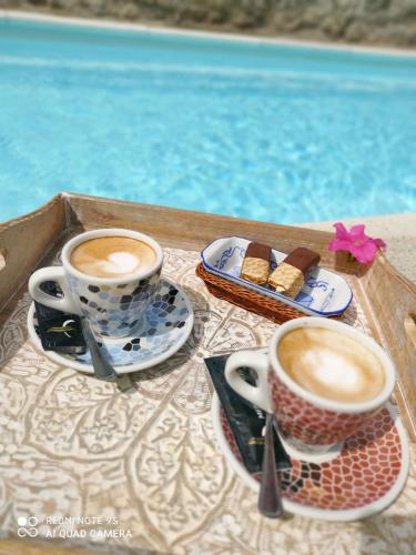two cups of coffee and cookies on a tray next to a pool at Posada Rural La Flor in Las Navas del Marqués