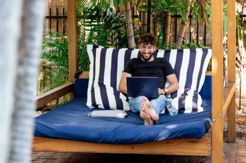 a man sitting on a bed with a laptop at Mad Monkey Central in Cairns