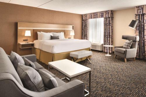 a hotel room with a bed and a couch and chairs at Wyndham Garden Conference Center Champaign - Urbana in Champaign