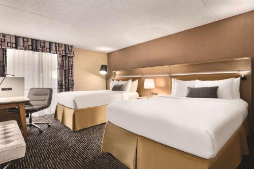 a hotel room with two beds and a desk at Wyndham Garden Conference Center Champaign - Urbana in Champaign