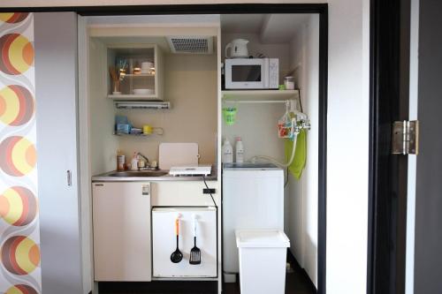 a small kitchen with white cabinets and a microwave at SUMIYOSHI APARTMENT Hotel 住吉アパートメントホテル in Fukuoka