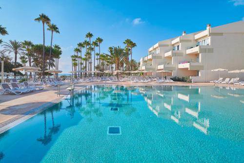 a swimming pool in front of a hotel with palm trees at Hipotels Mediterraneo Club in Sa Coma