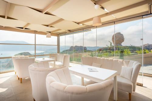 a dining room with white chairs and tables and large windows at White Rock of Kos Hotel - Adults only in Kefalos