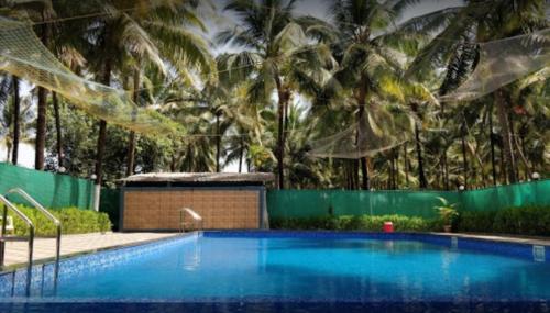 a large swimming pool with palm trees in the background at Madhuvan Farm cottage in Alibaug