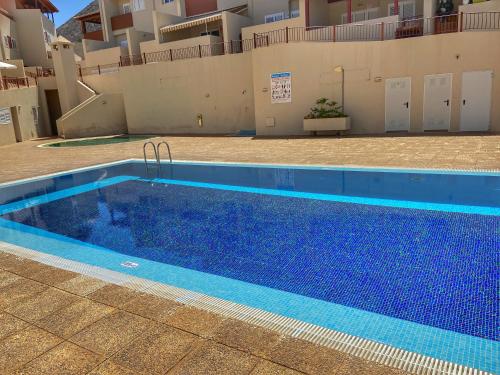 a large blue swimming pool next to a building at Los Cristianos 4 Bed Townhouse in Los Cristianos