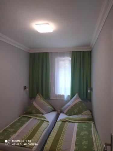 twee bedden in een kleine kamer met groene gordijnen bij Brill Apartman in Harkány