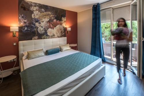 a woman is standing in a bedroom with a bed at Hôtel Les Jardins in Lucciana
