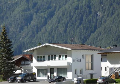 a building with cars parked in front of a mountain at Apart Crystal in Längenfeld